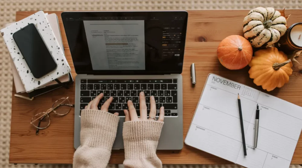 Rédactrice web tapant sur un ordinateur portable avec un agenda et des notes
