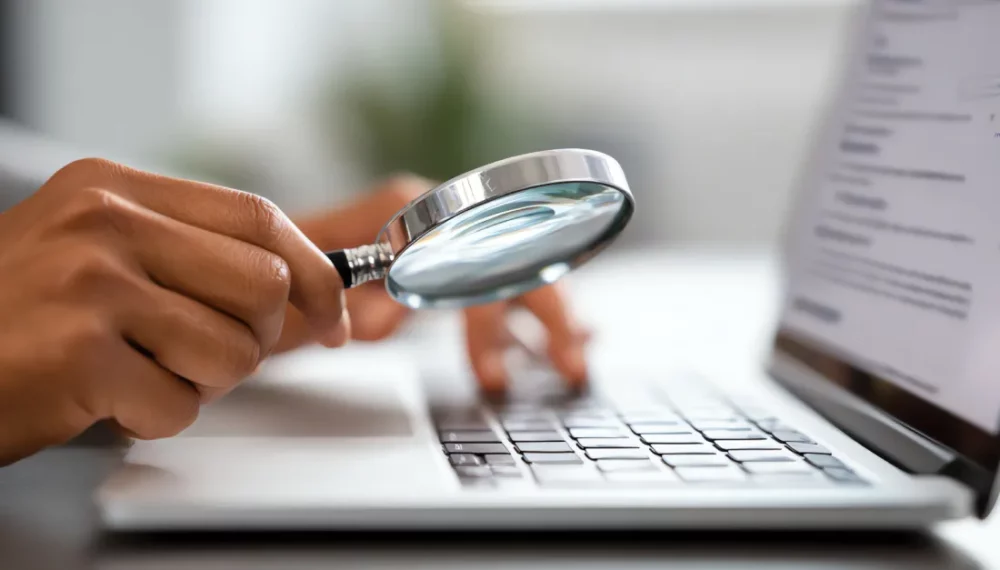 Loupe tenue devant un clavier d'ordinateur pour illustrer la recherche de mots-clés