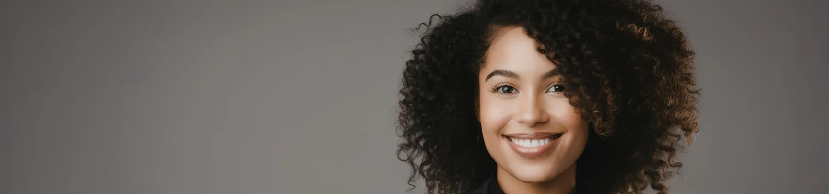 femme au cheveux bouclés souriante qui pose en tailleur noir pour illustrer comment rédiger une page à propos efficace
