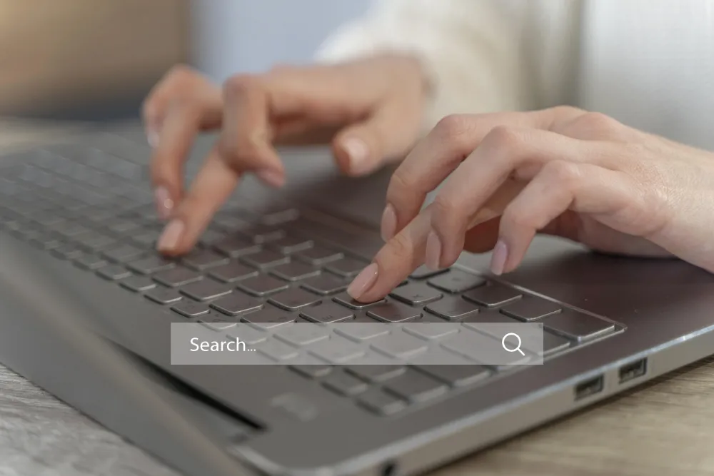 Mains tapant sur un clavier avec une barre de recherche illustrant les intentions de recherche SEO