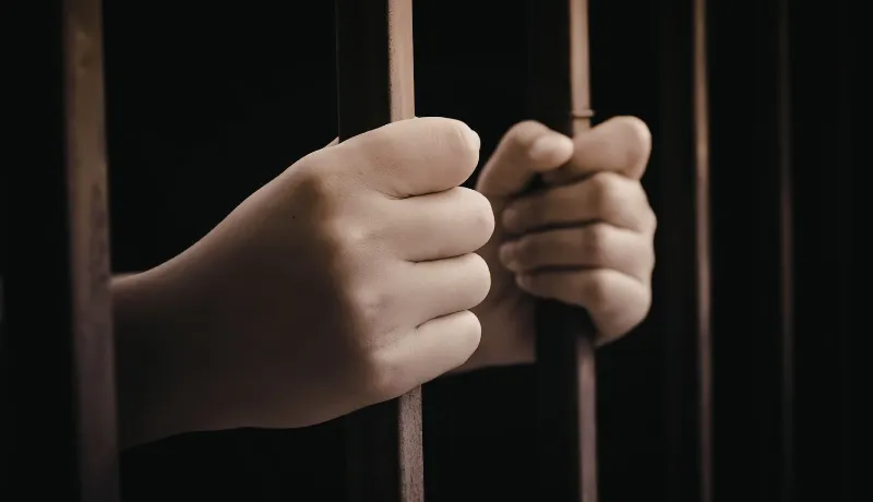 deux mains qui tiennent des barreaux d'une prison